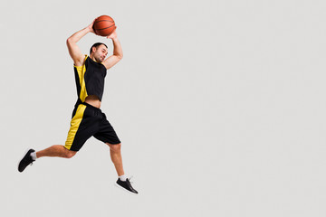 Side view of basketball player posing mid-air while throwing ball with copy space