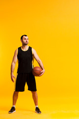 Fototapeta na wymiar Front view of basketball player posing with ball close to hip and copy space