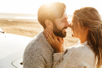 Happy young couple in love embracing while leaning on a car