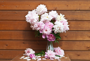 Beautiful bouquet of pink peonies in a glass vase against the background of the wooden wall of a summer arbor. Summer garden vacation. Flower rustic still life