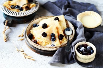 Thin pancakes with blueberries and condensed milk on a plate on a gray background