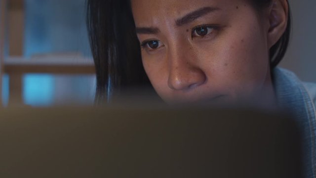 Millennial young Chinese businesswoman working late night stress out with project research problem on laptop in living room at modern home. Asia people occupational burnout syndrome concept.