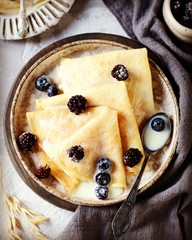 Thin pancakes with blueberries and condensed milk on a plate on a gray background