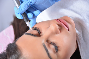 Cosmetologist applying permanent makeup on eyes on the beautiful girl in beauty studio. Eyeliner tattoo with a professional tool. Close up, selective focus