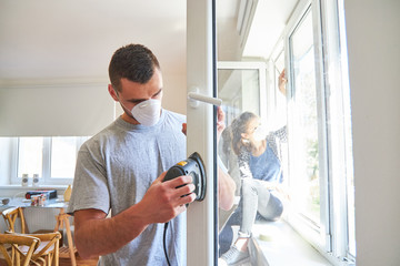Junger Mann als Heimwerker beim Fenster abschleifen