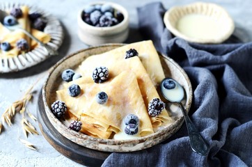 Thin pancakes with blueberries and condensed milk on a plate on a gray background