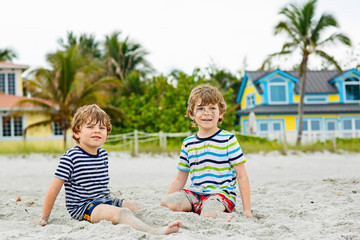 Two little kids boys having fun with building a sand castle on tropical beach of Miami beach, Florida children playing together on their vacations