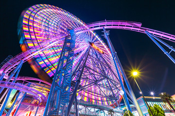 Bottom view of colorful giant Ferris Wheel and Roller Coaster illuminated at night in Minato Mirai...
