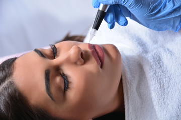 Cosmetologist applying permanent makeup on woman lips in beauty studio with a professional tattoo tool. Beauty and micro pigmentation concept. Close up, selective focus