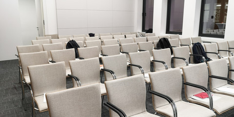 Several rows of empty gray fabric-covered chairs in a light-lit room for business training seminars or meetings with large evening windows.Concept of fear of public speaking,training oratorical skills