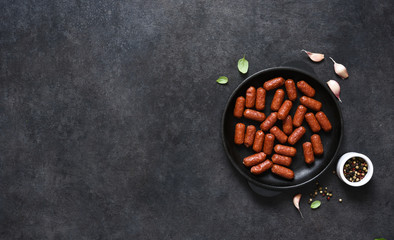 Spicy chorizo sausages in a cast-iron pan on a black background with place for text.