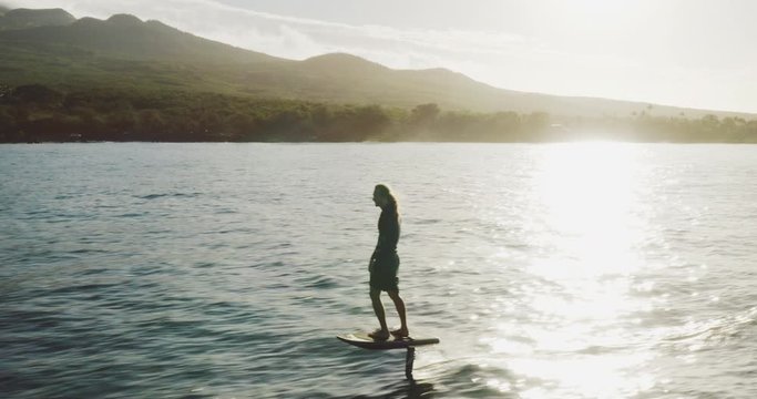 Aerial view following a man on an electric hydrofoil personal water craft surfboard riding in the ocean at sunrise, the future of electric water transportation and vehicles