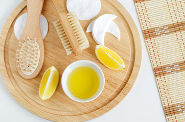 Fototapeta na wymiar Lemon juice and slices, cotton pads, wooden hairbrush and body brush. Ingredients for preparing homemade mask. Natural beauty treatment recipe and zero waste concept. Top view, copy space. 