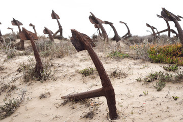 Rusty old anchors on the beach at the Anchor Cemetary graveyard at Praia do Barril beach, in Tavira, Algarve, Portugal