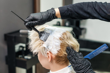 Hairdresser applies white dye on woman's hair in beauty salon.