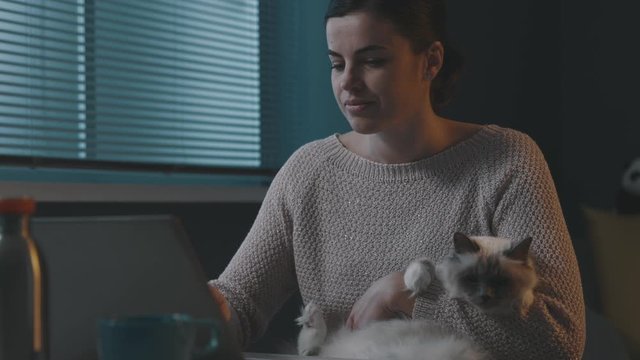 Woman holding her cat and using her laptop