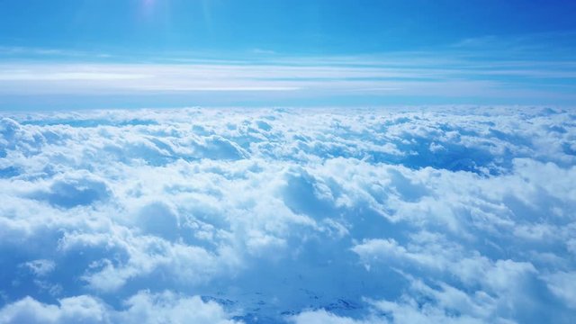 Fluffy clouds in the blue sky seen from an airplane. Under the snowy mountains.