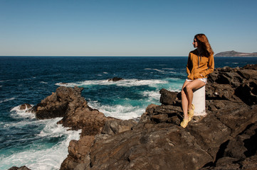 Cute girl in stylish clothes sitting on rocky coast