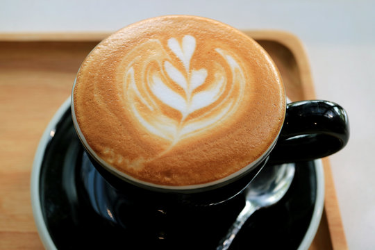 Cup of cappuccino coffee with latte art on a wooden tray