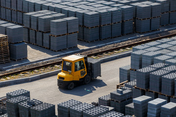 Industrial photography. A yellow forklift rides through a warehouse past pyramid-packed packages of...