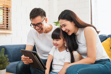 Happy Asian family spending time together at sofa/home playing game, tablet for education