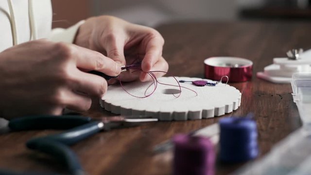 Lifestyle concept, work from home to reinvent your life: close-up of woman hands making macrame woman burns the wire with the appropriate tool to finish the job on kumihimo tools on wooden table