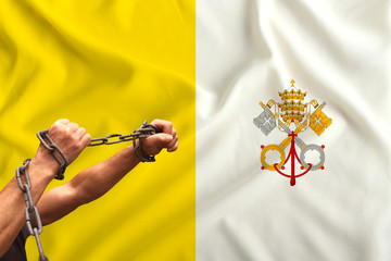 male hands of a prisoner in iron chains against the background of the national flag of Vatican on...