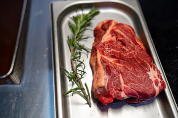 Raw meat with rosemary on a metal tray.