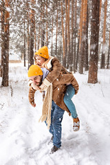 Girl having fun riding on her man in winter forest at the snowfall