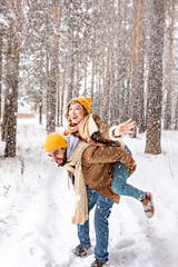 Girl having fun riding on her man in winter forest at the snowfall