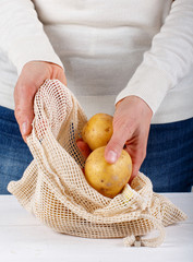 Woman put fresh potatoes in a textile bag