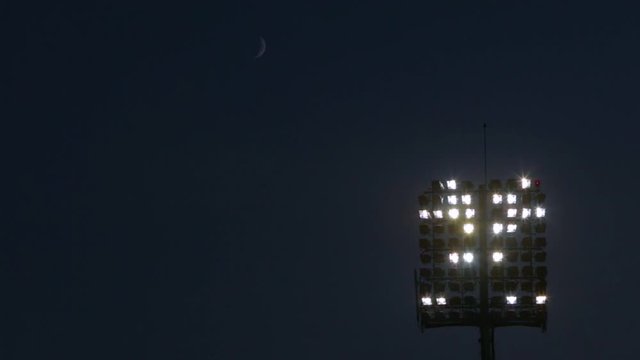 Light Tower Lit At A Stadium During Nighttime And A New Moon