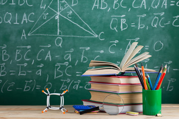 Education and sciences concept - books on the teacher desk in the auditorium, chalkboard on the background.