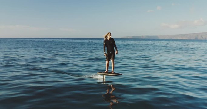Aerial view of a young man riding on an electric hydrofoil surfboard on glassy blue ocean water, the future of green electric personal watercraft is hydrofoiling