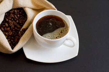 coffee beans in a bag with a white Cup of fresh coffee on a black background. space for text, top...