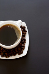 coffee beans in a bag with a white Cup of fresh coffee on a black background. space for text, top view.