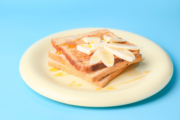 Tasty toasted bread with honey, butter and banana on color background