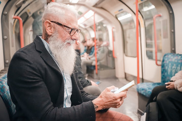 Pensioner playing with cellular phone sitting his train. Entrepreneur man using smartphone in subway underground. high iso. Holiday, work and lifestyle concept - Image