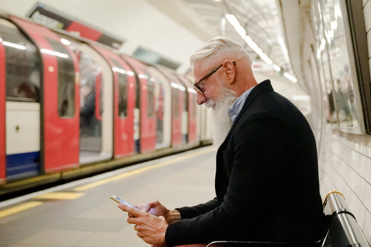 Pensioner playing with cellular phone waiting his train. Entrepreneur man using smartphone in subway underground. high iso. Holiday, work and lifestyle concept - Image