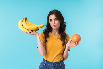 Thoughtful woman choosing between bananas and orange.