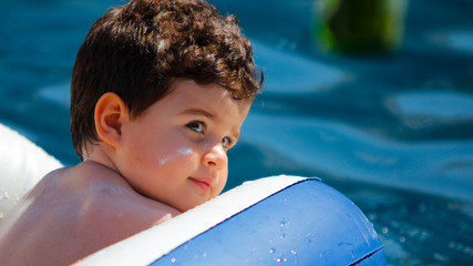 criança de protetor solar no rosto brincando com boia na piscina