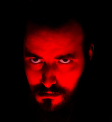 bearded boy with red light on his face worrying fear and tyrant look.