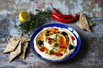 Hummus served on a blue plate with olives, seasonings and olive oil. Vegan plate.