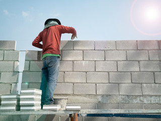 Bricklayer is working on Scaffolding, COOL BLOCK is made of concrete together with EPS in the middle of concrete block, lens flare on right top on photo