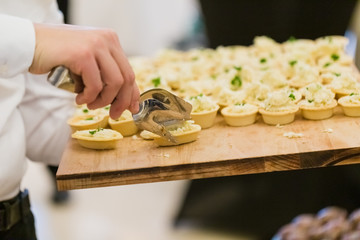 Waiter scooping finger food canapes from wooden plate with utensil tong at celebration event.