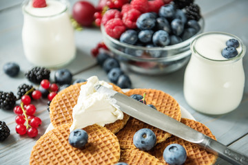  Different types of ripe berries - blueberries, raspberries, red currants, mulberries, a drink from berries and waffles with cheese. Appetizing snack with berries. Jars of natural yogurt.