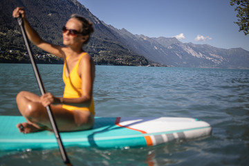 Pretty, young woman paddling on a paddle board on a lake, enjoying a lovely summer day