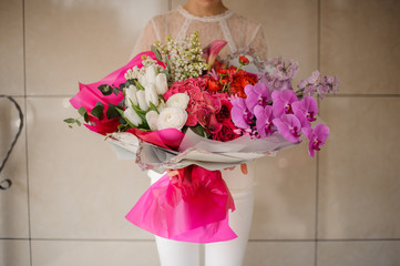 Girl holding a huge spring bouquet of different white, red, pink and rose color flowers wrapped in paper