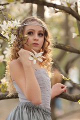  young beautiful blonde in a silver dress with a train in the spring garden, where white magnolia blooms, close-up