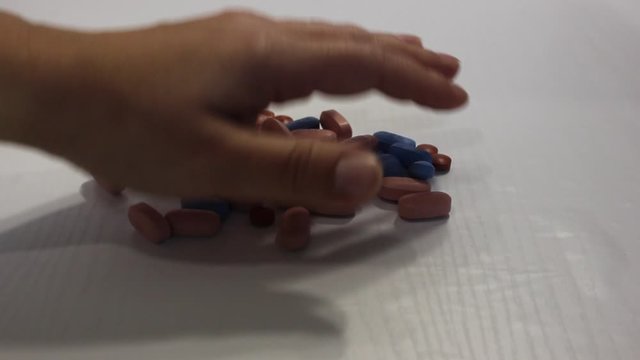 Pills isolated on white. Social problems of drugs and HIV. Brown, blue medicine. Hand picks up the pills. Hand raking a handful of drugs.